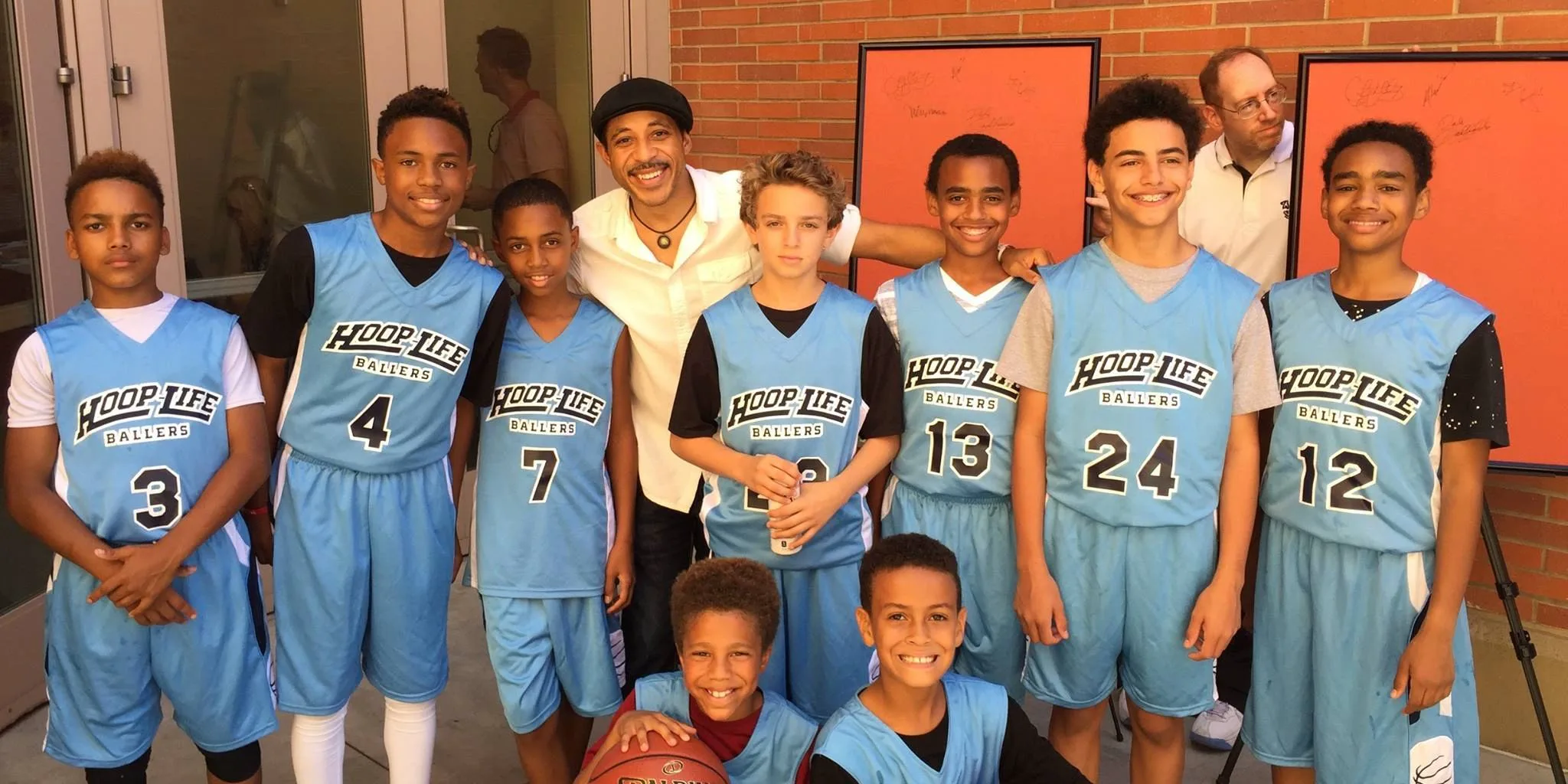 A youth basketball team in Hoop Life Ballers jerseys posed with an adult outside a gym