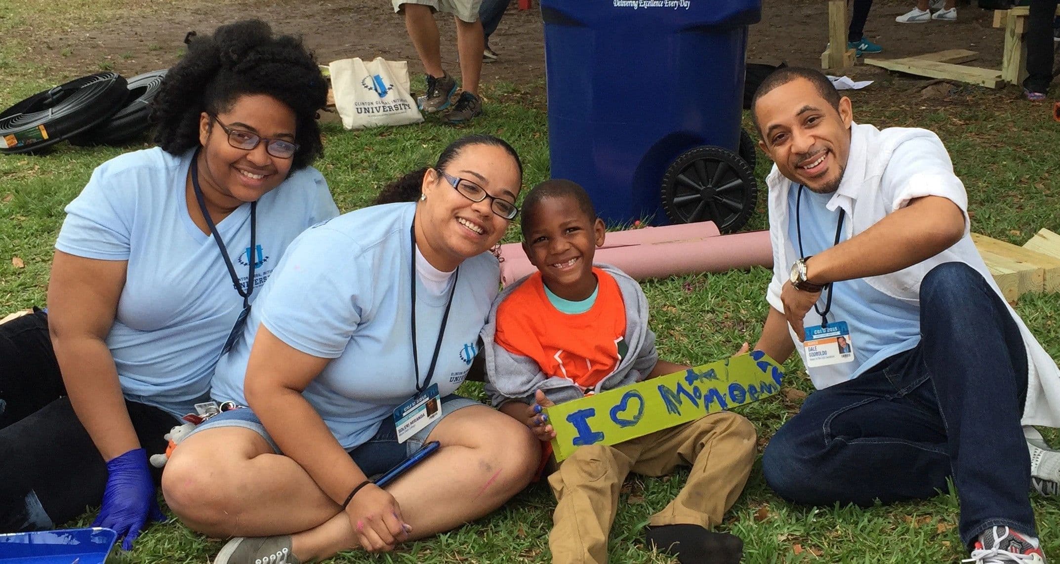 Four volunteers in matching shirts outdoors with a young boy