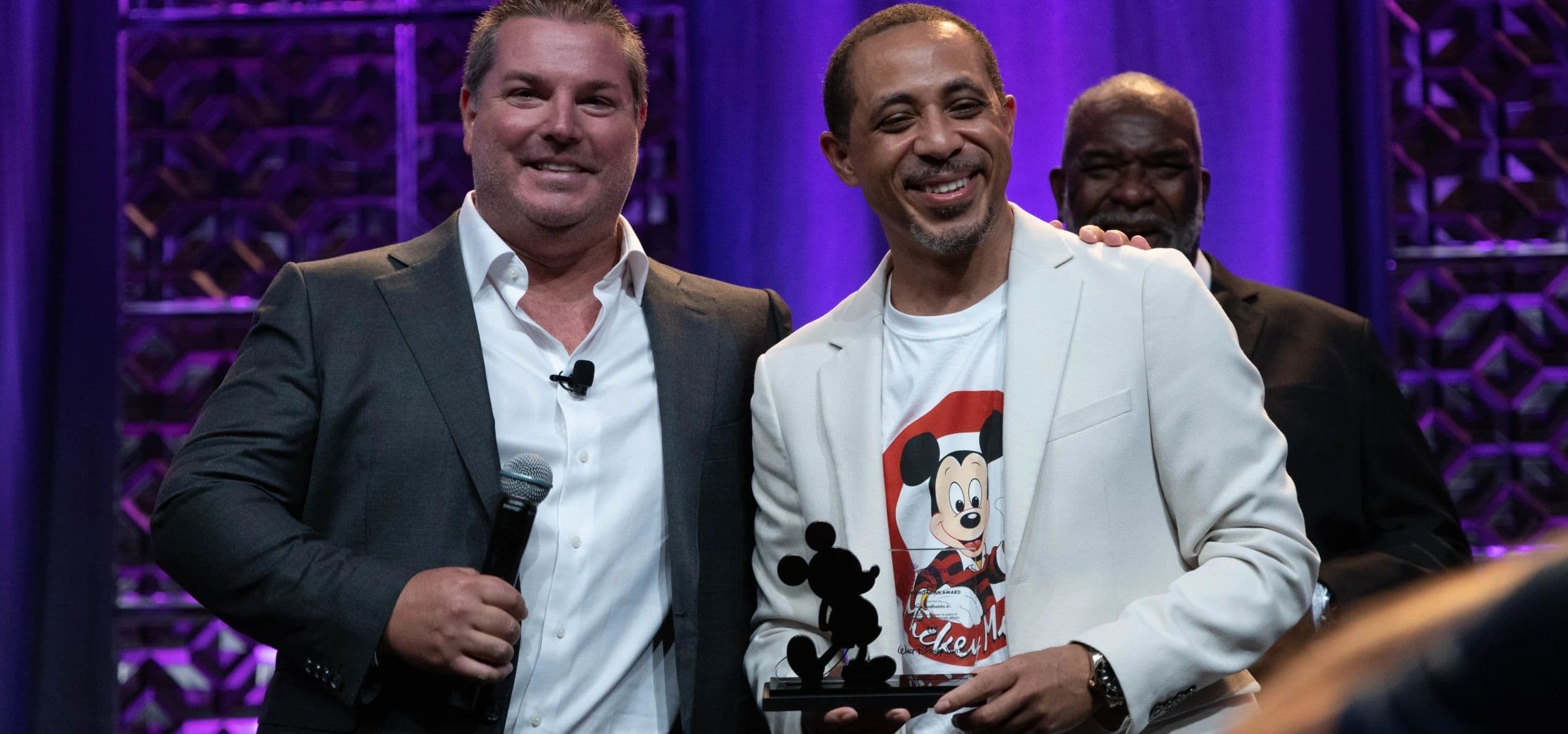 Two men on stage, one holding a statuette award