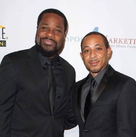 Two men in black tie at a sports marketing event backdrop
