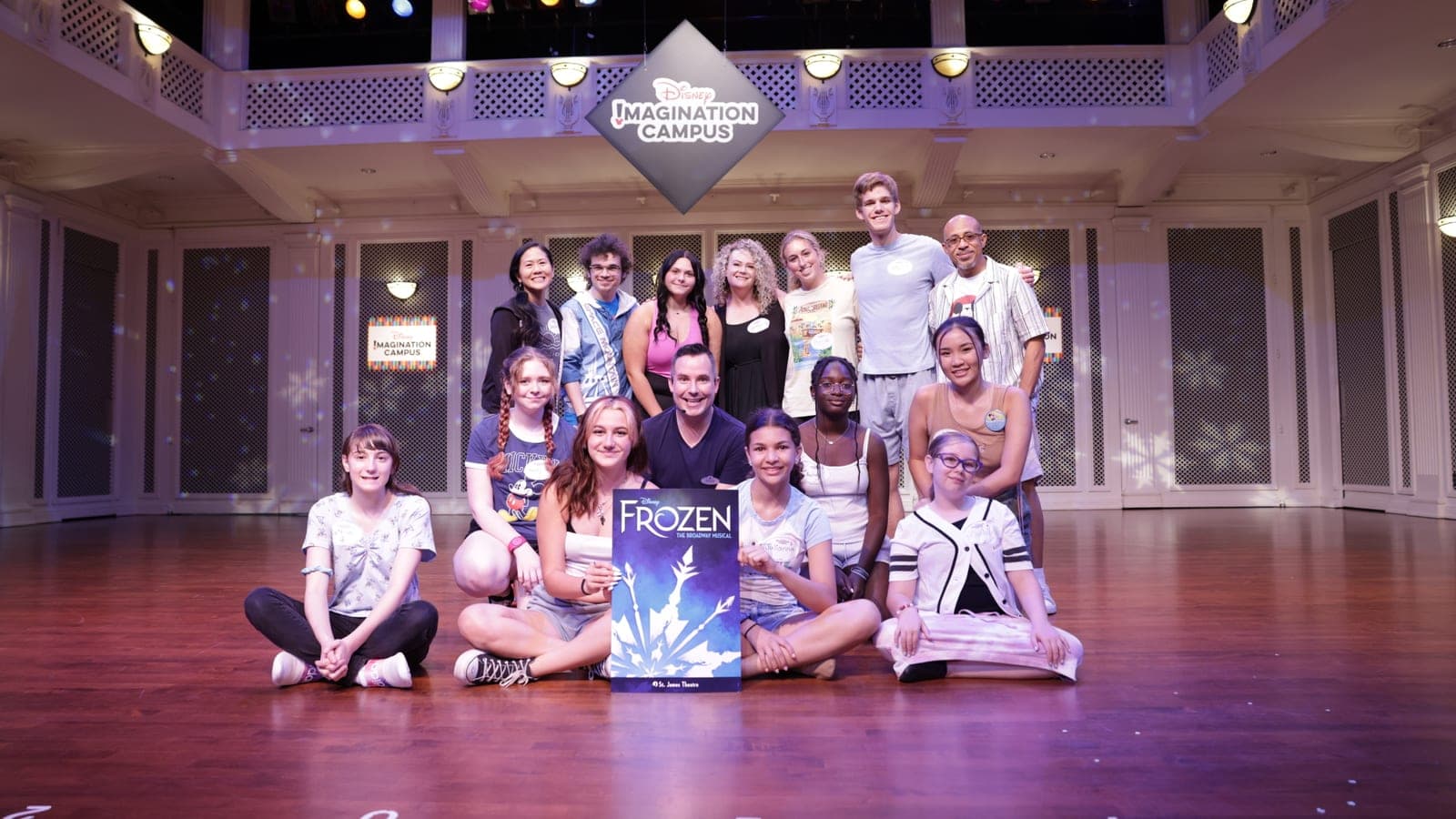 A group posed on a theatre stage beside a Frozen poster