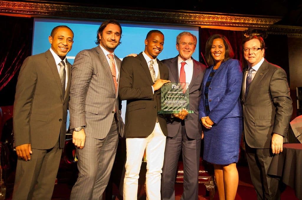 Six people on stage at an awards presentation, holding a glass award