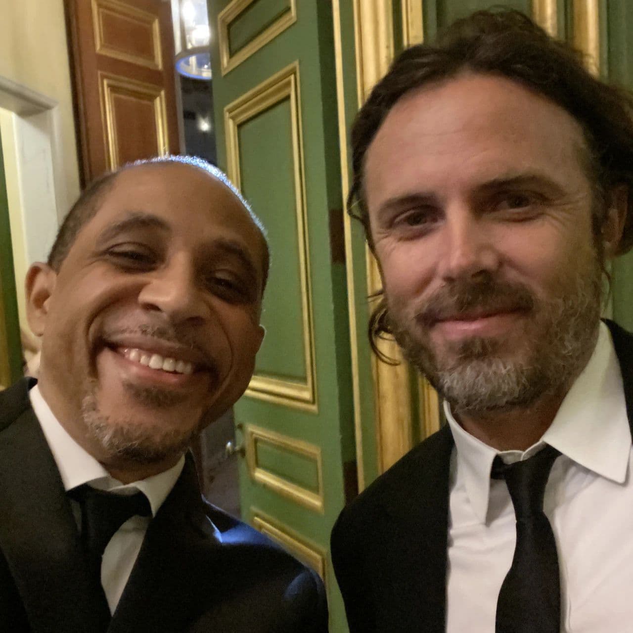 Two men in black tie in front of ornate green and gold doors